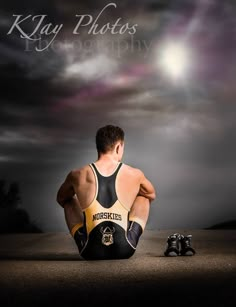 a man sitting on the ground with his legs crossed in front of him, wearing a black and yellow wrestling suit