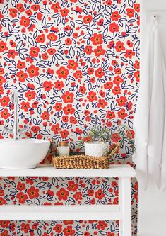 a white sink sitting under a bathroom mirror next to a flowery wallpaper covered in red and blue flowers