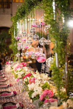 a long table is decorated with pink and white flowers, greenery and hanging ornaments