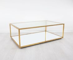 a glass and brass coffee table with mirrored shelves on the bottom, against a white wall