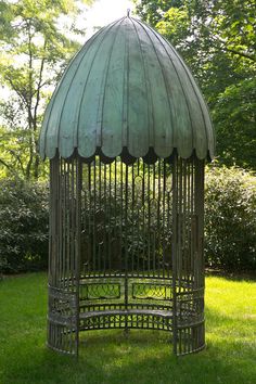 a metal birdcage sitting on top of a lush green grass covered park area