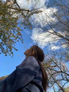 a woman standing in front of trees looking up at the sky