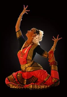 a woman in an orange and gold outfit is doing some kind of dance move with her hands up