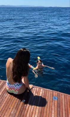 a woman sitting on top of a wooden pier next to a child in the water