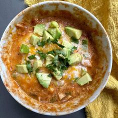 a white bowl filled with soup and topped with avocado