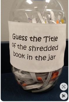 a glass bowl filled with lots of different types of paper and scissors next to a sign that says guess the title of the shredded book in the jar