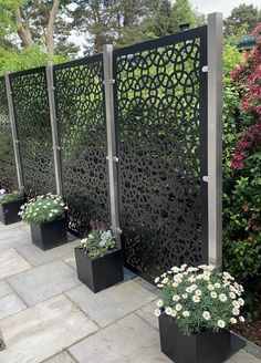 four black planters with flowers in them are lined up on the side of a sidewalk