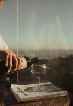 a person pouring wine into a glass on top of a table with a book and magazine