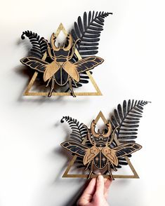 two pieces of art made out of wood and metal with designs on them, one being held by a person's hand