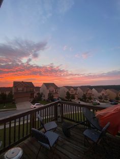 the sun is setting over some houses and lawn chairs on a deck with an umbrella