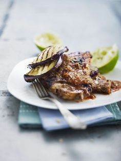 a white plate topped with meat covered in sauce next to sliced bananas and apple slices