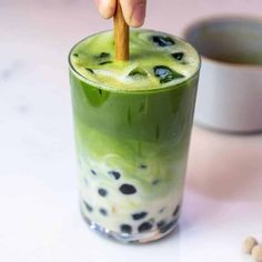 a hand holding a wooden stick above a green drink with black dots on the rim