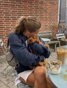 a woman sitting at a table with a dog in her lap and eating cereal from a bowl