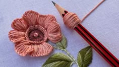 a pencil and flower on a piece of cloth next to a crochet hook