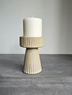 a white candle sitting on top of a cement table next to a wall and floor