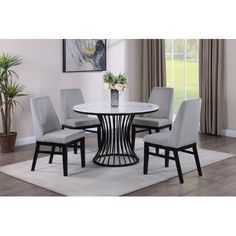 a round dining table with four chairs and a plant in the middle on a rug