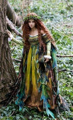 a woman with long red hair and green dress standing next to a tree in the woods