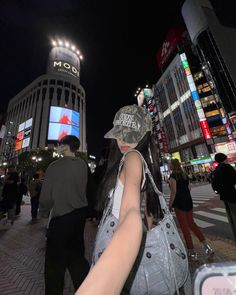 a woman is standing in the middle of a busy city at night with her hand on her hip