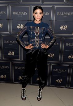 a woman standing in front of a wall wearing black pants and heels with her hands on her hips