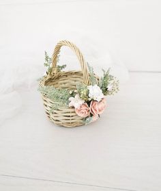 a wicker basket with flowers and greenery on the inside is sitting on a white surface