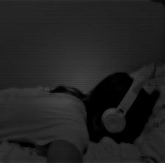 a black and white photo of a cat laying on a bed with its head down