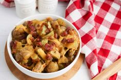 a white bowl filled with pasta and meat on top of a wooden cutting board next to a red checkered table cloth