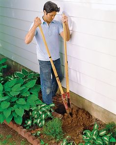 a man is holding two shovels and digging in the ground next to a house