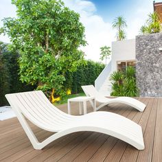 two white lounge chairs sitting on top of a wooden deck next to a wall and trees