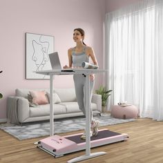 a woman standing at a desk with a laptop computer on top of it in front of a pink wall