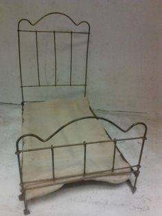 an old iron bed frame with white sheets on the headboard and foot board, sitting against a wall