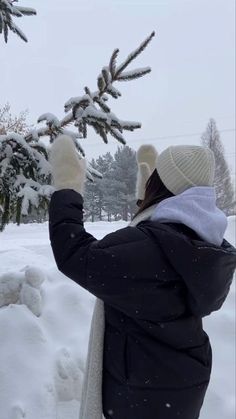 a woman is standing in the snow with her hand up to a pine tree branch