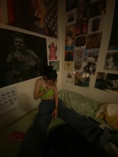 a woman sitting on top of a bed next to a wall covered in pictures and posters