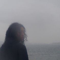 a woman standing on top of a beach next to the ocean under a cloudy sky