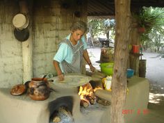 a woman is making food on an outdoor stove in a hut with pots and pans