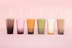 five different colored cups with straws lined up in a row on a pink background