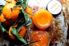 two jars of orange juice sit on a table next to some oranges and leaves