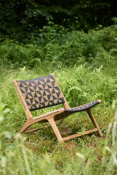 a wooden chair sitting on top of a lush green field next to tall grass and trees