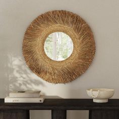 a round mirror hanging on the wall above a console table with books and vases