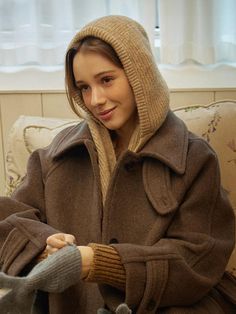 a woman sitting on a couch wearing a brown coat