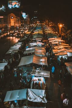 an outdoor market with lots of tents and people walking around it at night in the city