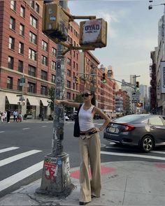 a woman standing next to a traffic light on the side of a road with buildings in the background