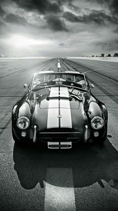 a black and white photo of a sports car on the tarmac with clouds in the background