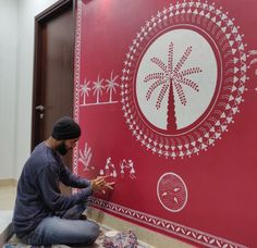 a man sitting on the floor in front of a red wall with palm trees painted on it