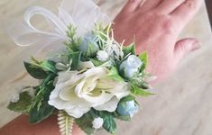 a wrist corsage with white flowers and greenery on the wrist is being held by someone's hand