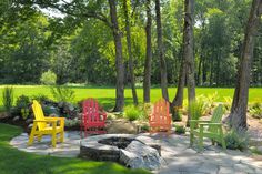 four colorful chairs sitting around a fire pit in the middle of a park with grass and trees