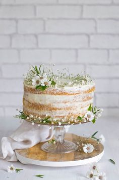 a three layer cake with flowers and greenery on top, sitting on a wooden platter