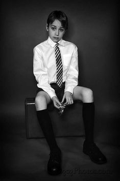 black and white photograph of a young boy in dress clothes sitting on a suitcase with his legs crossed