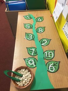 a wooden table topped with lots of green leaves and numbers painted on the top, next to a bowl of peanuts