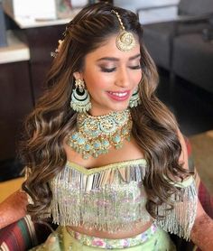 a woman with long hair wearing a green dress and gold jewelry on her head, sitting in