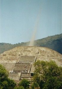 an ancient structure in the middle of some trees and hills with a rainbow coming out of it